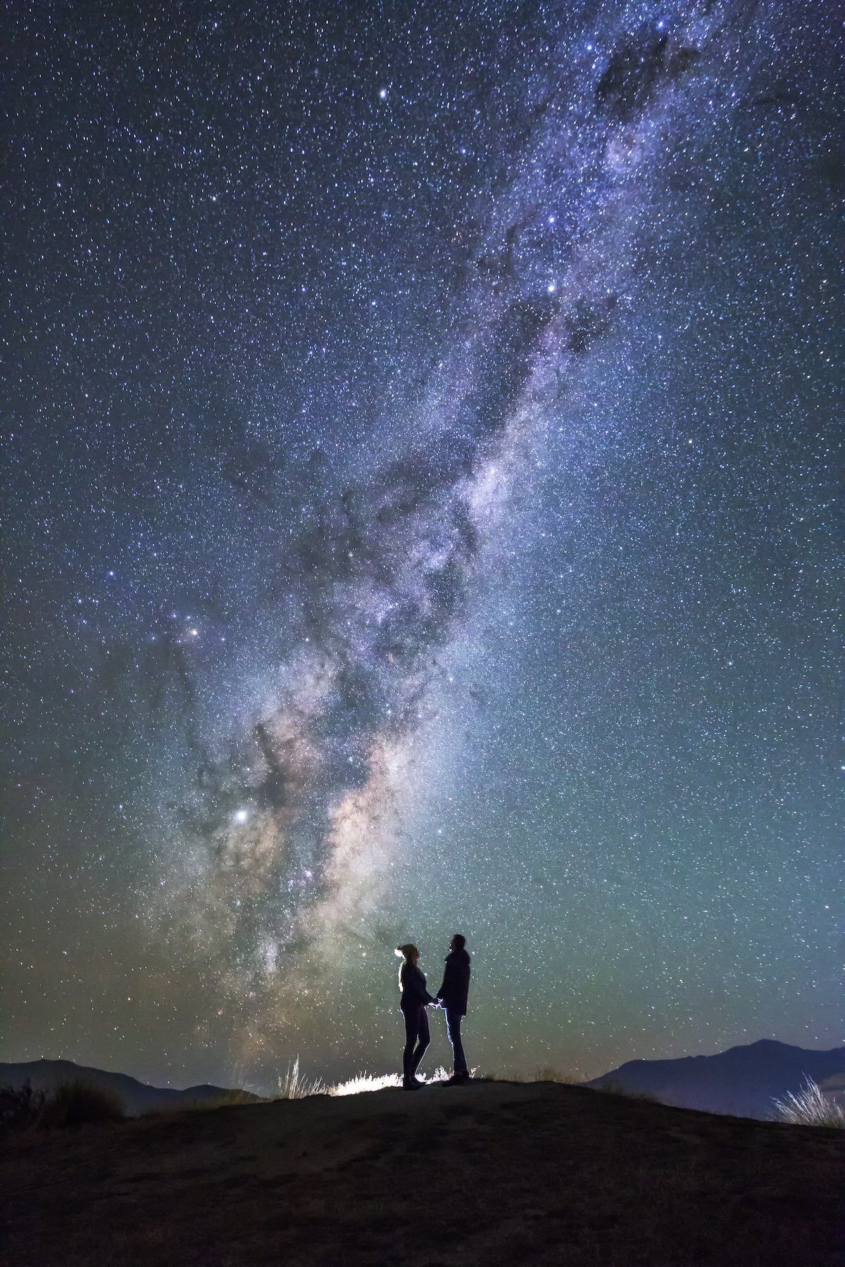 Astrophotography picture of a couple eloping on a hill at night under the stars.