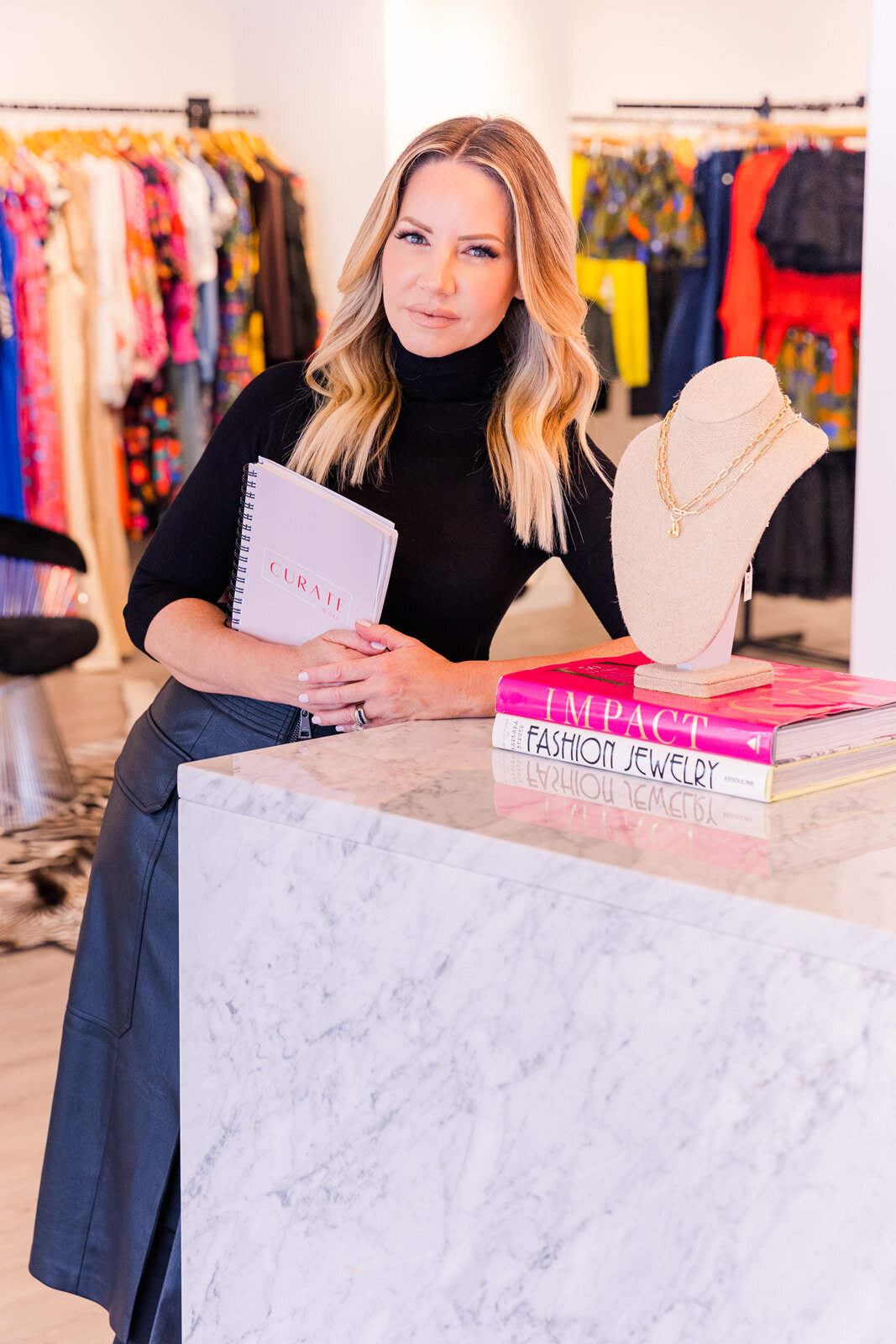 stylist standing next to a fashion store counter holding branded notbook and wearing black turtleneck  Atlanta personal brand photographer | Laure Photography branding