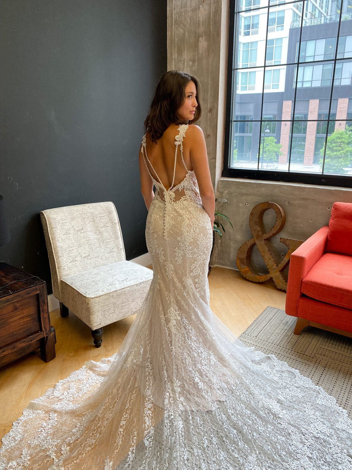 An elegant model poses in an open back wedding dress with a dramatic train in a modern studio.
