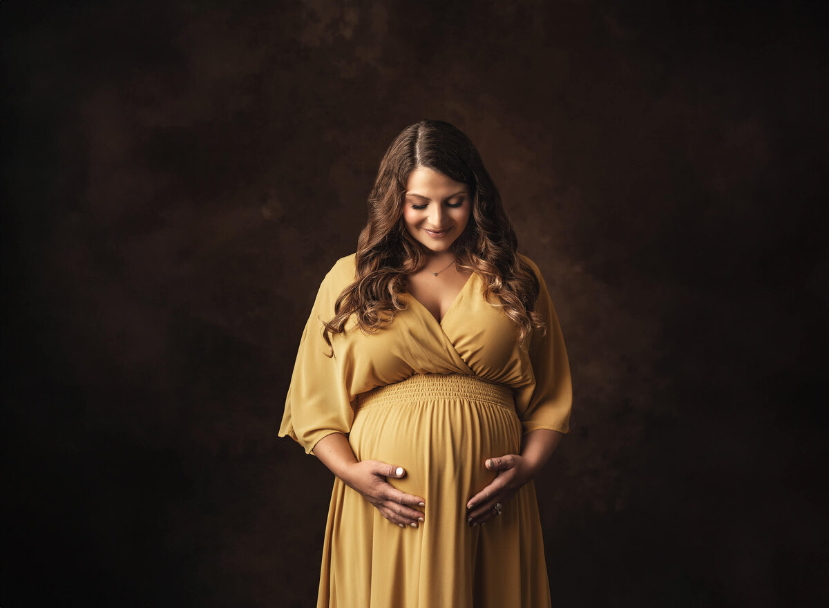 Woman in golden dress holding her baby bump looking down in Fairhope, Alabama