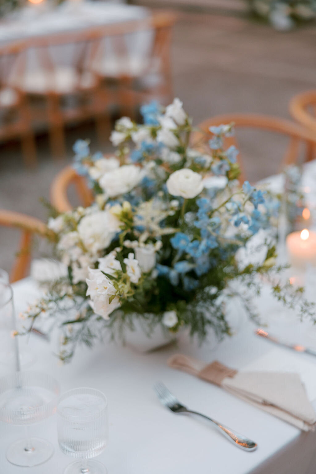 Dusky lighting with reception tables having blue and white florals on top in a courtyard