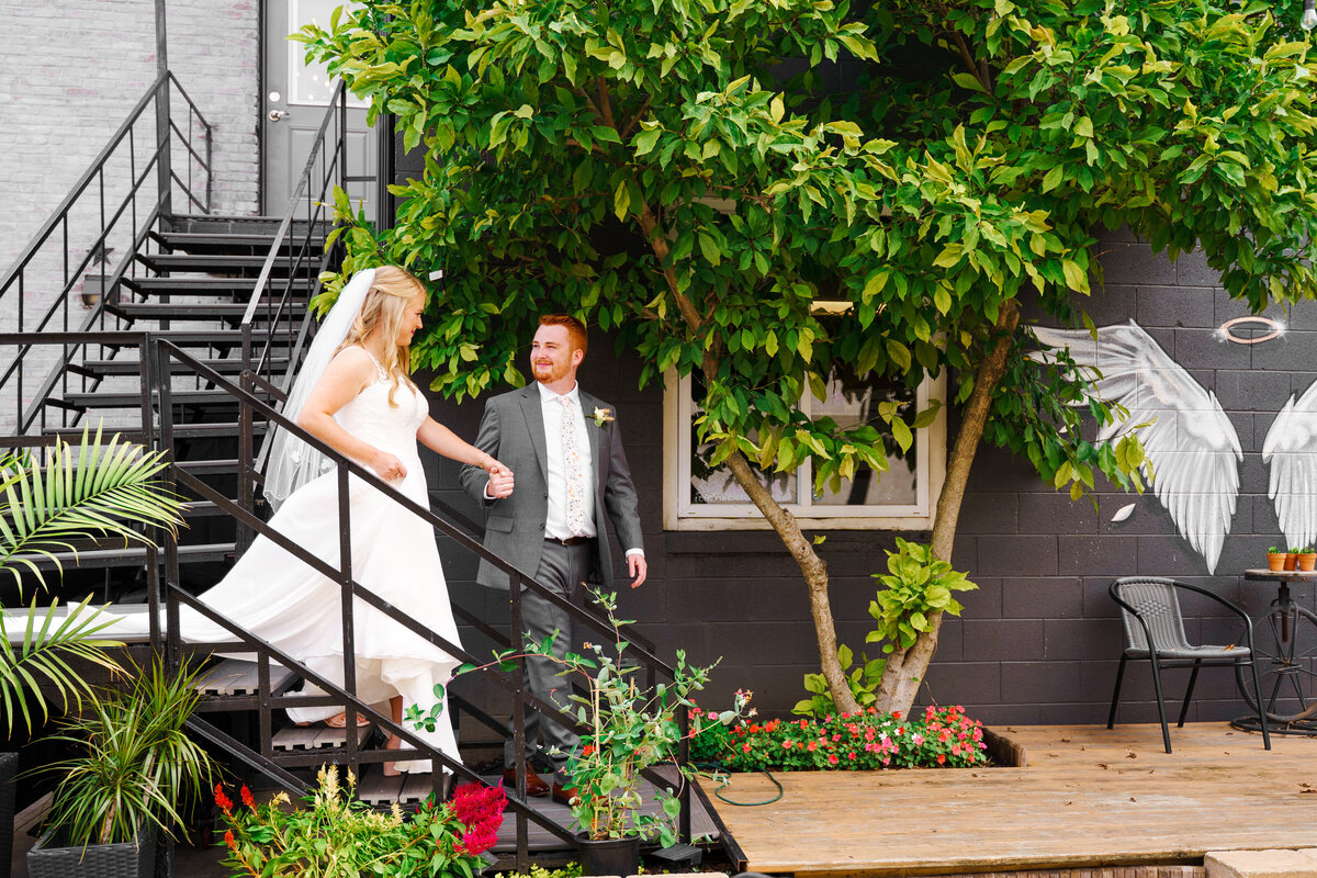Groom leads his bride down some black, metal stairs outside their wedding at 1883 Locale in Reynoldsburg, Ohio.