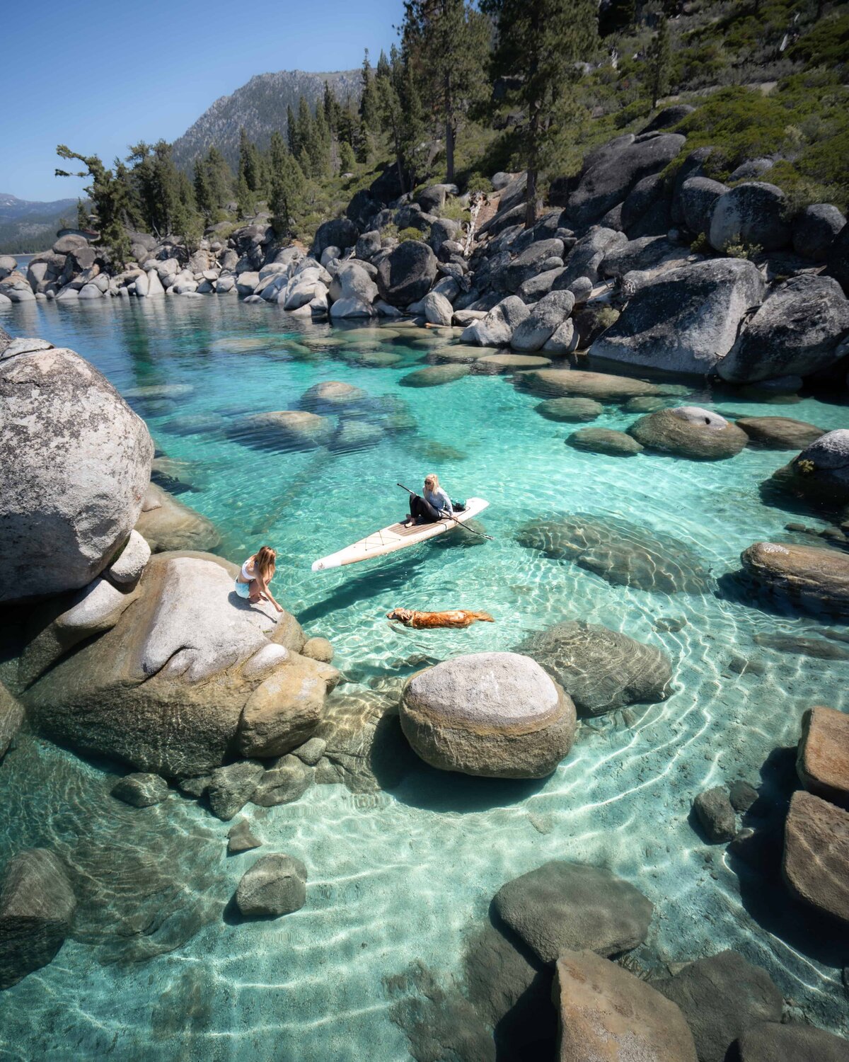 Jess of Jess Wandering kayaking on Lake Tahoe with rocks under the water and mountains in the background