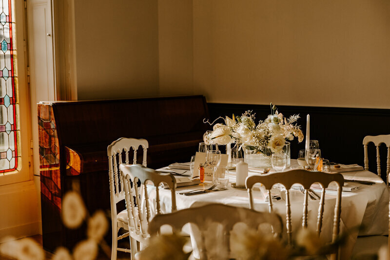 Table de mariage tout en blanc dans un coin de salle baignée par lumière perçant par la fenêtre. Scène immortalisée par Laura, photographe de mariage en Vendée.