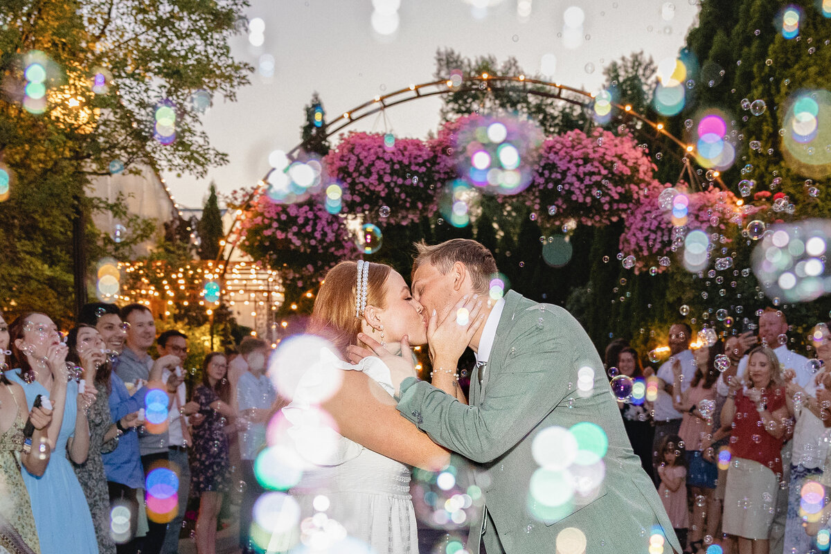 The newlyweds embrace and kiss during their grand exit as guests blow bubbles, creating a dreamy and colorful nighttime farewell scene.