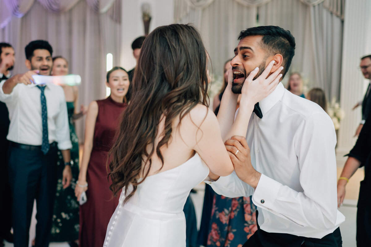 Black and white photo of a bride wearing a strapless dress with a bow and groom with a black tie tux walk hand in hand. Photo by Anna Brace, an Omaha wedding photographer.