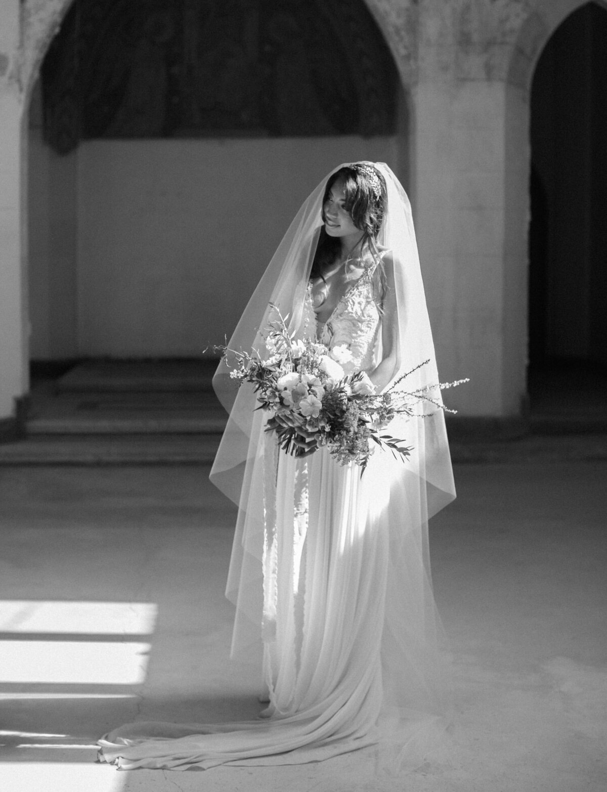 natural, candid black and white film wedding photographer in Italy, bride with long veil in sunlight, abandoned cathedral