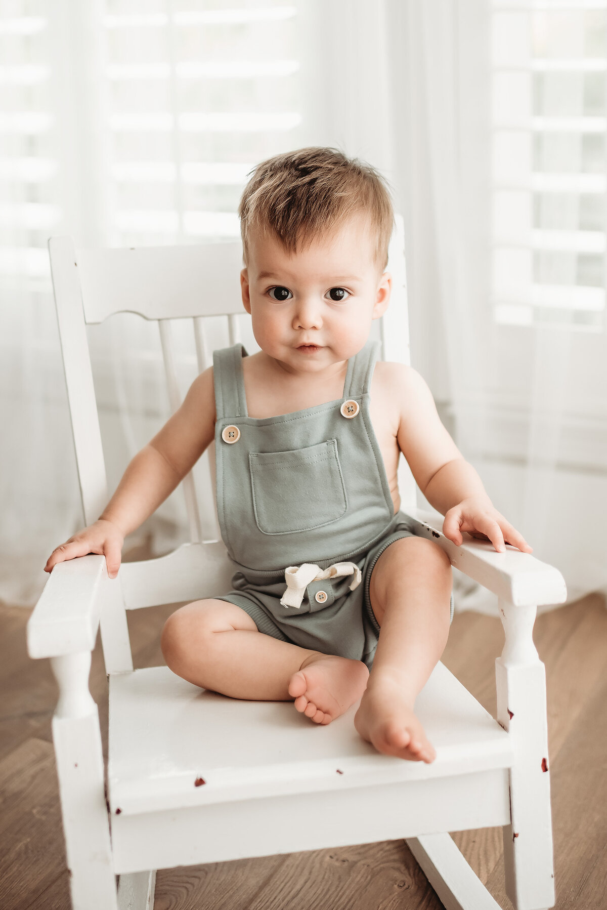 baby boy sitting in white rocking chair in denver photographer's studio