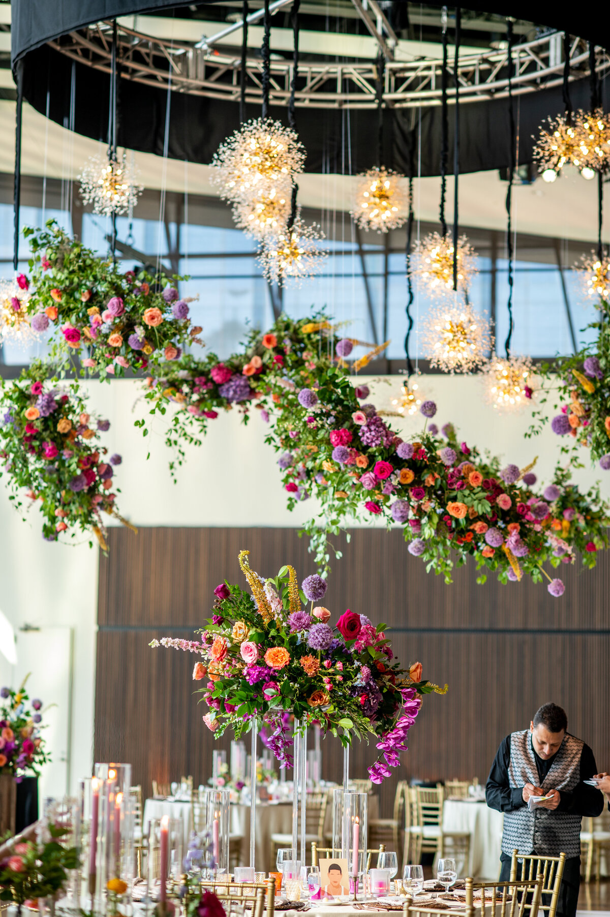 Joyful hanging floral cloud chandelier installation composed of petal heavy roses, allium, eremurus, delphinium, snapdragons, spray roses and garden-inspired greenery in hues of pink, fuchsia, lavender, orange, and golden yellow lighting up the dance floor of this summer wedding. Design by Rosemary and Finch in Nashville, TN.
