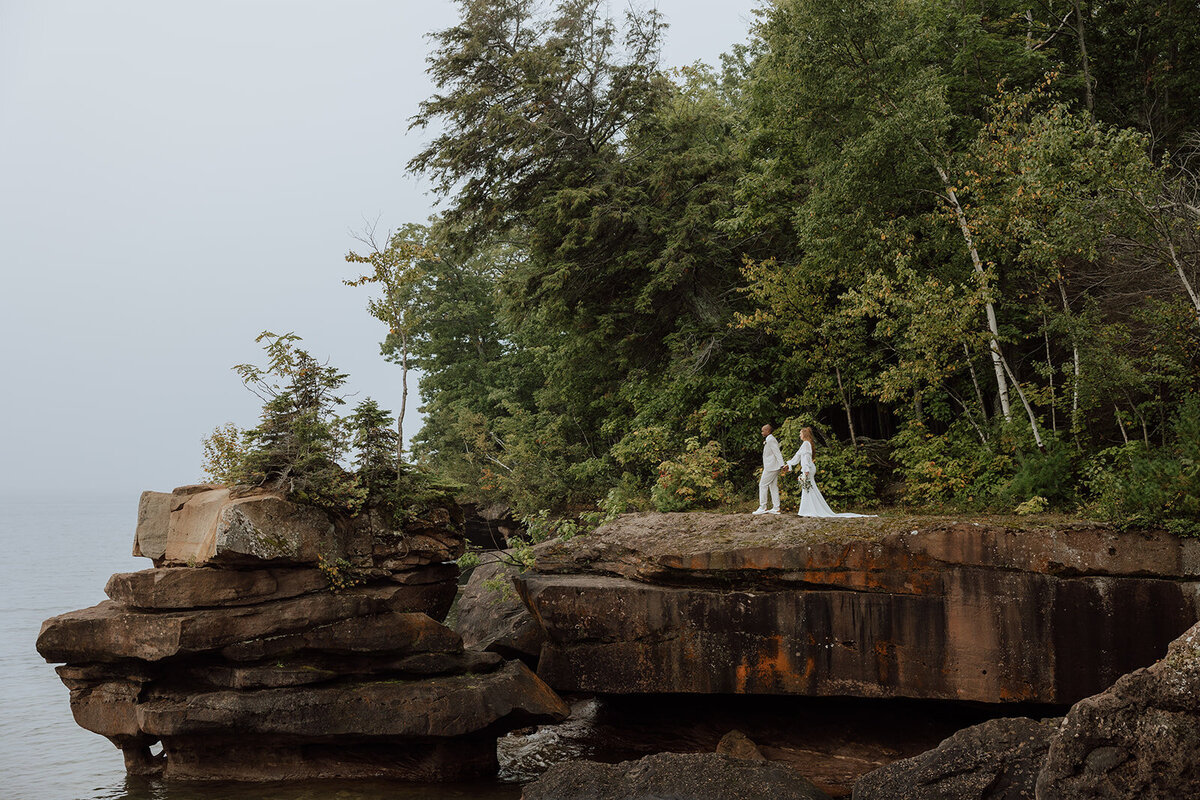 Bride and groom standing on a rock over lake superior on Madeline Island. Photo taken by a Wisconsin Elopement Photographer