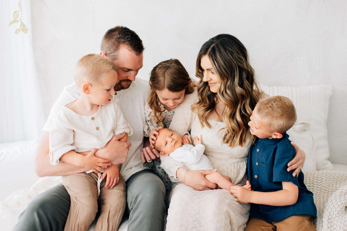 family of six snuggling together looking at the newest baby in mom's arms