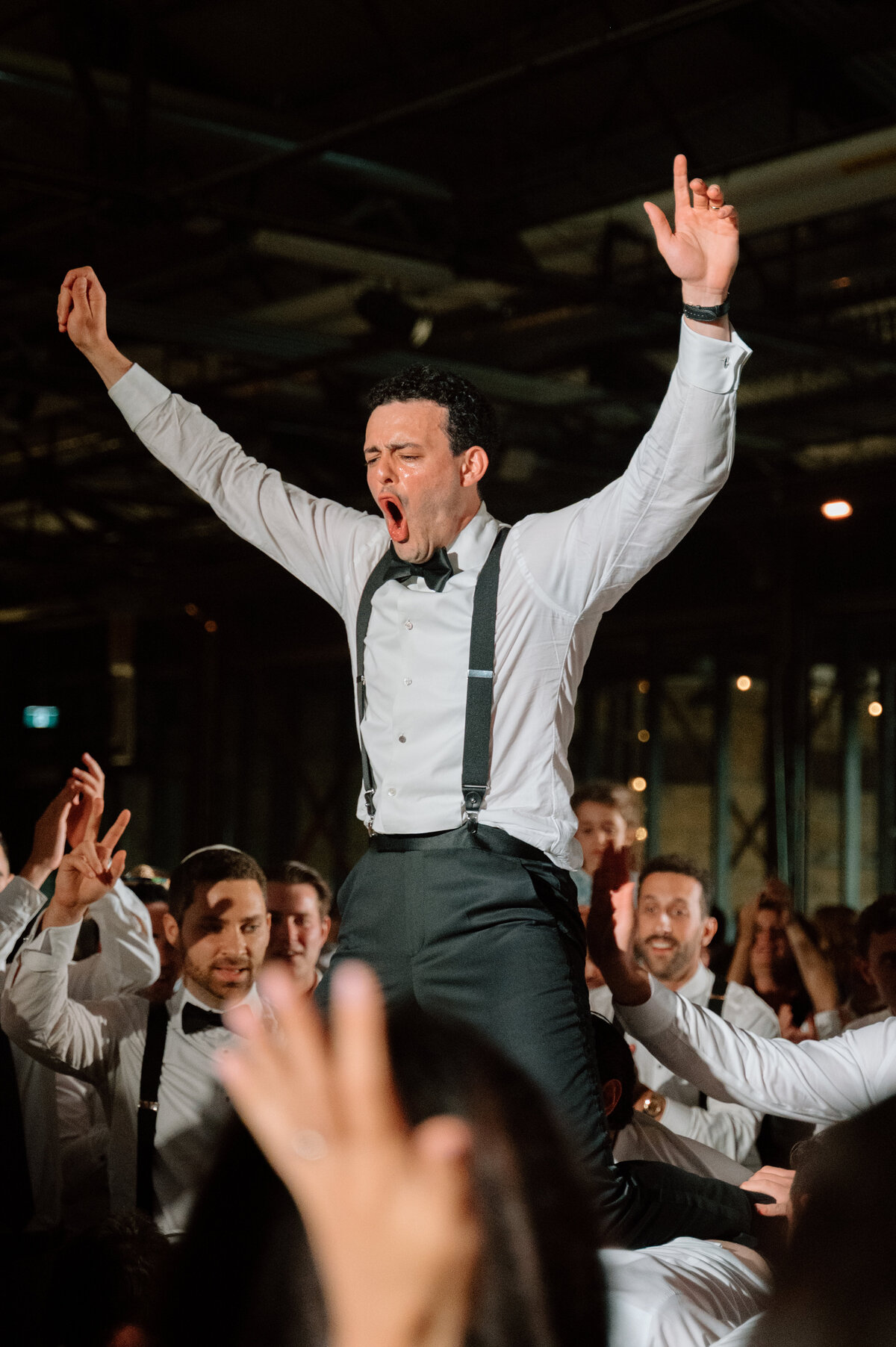 Groom dancing energetically at hora dance with arms raised during the party.