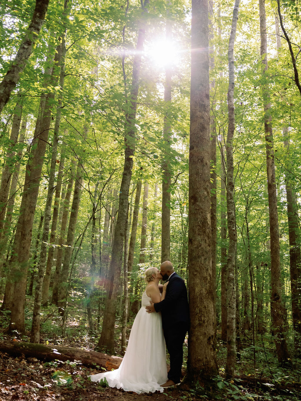 Bride and groom sharing an intimate moment in the sun-dappled forest at Greenbrier during their eloping to Gatlinburg ceremony, surrounded by tall trees and natural light filtering through the leaves.
