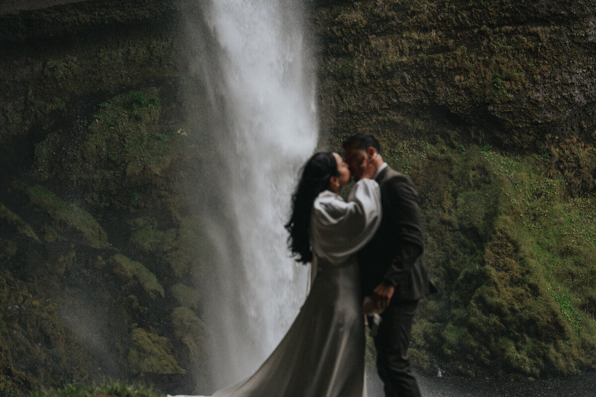 Husband and wife kiss by a secluded waterfall in Iceland after exchanging vows during their elopement 
