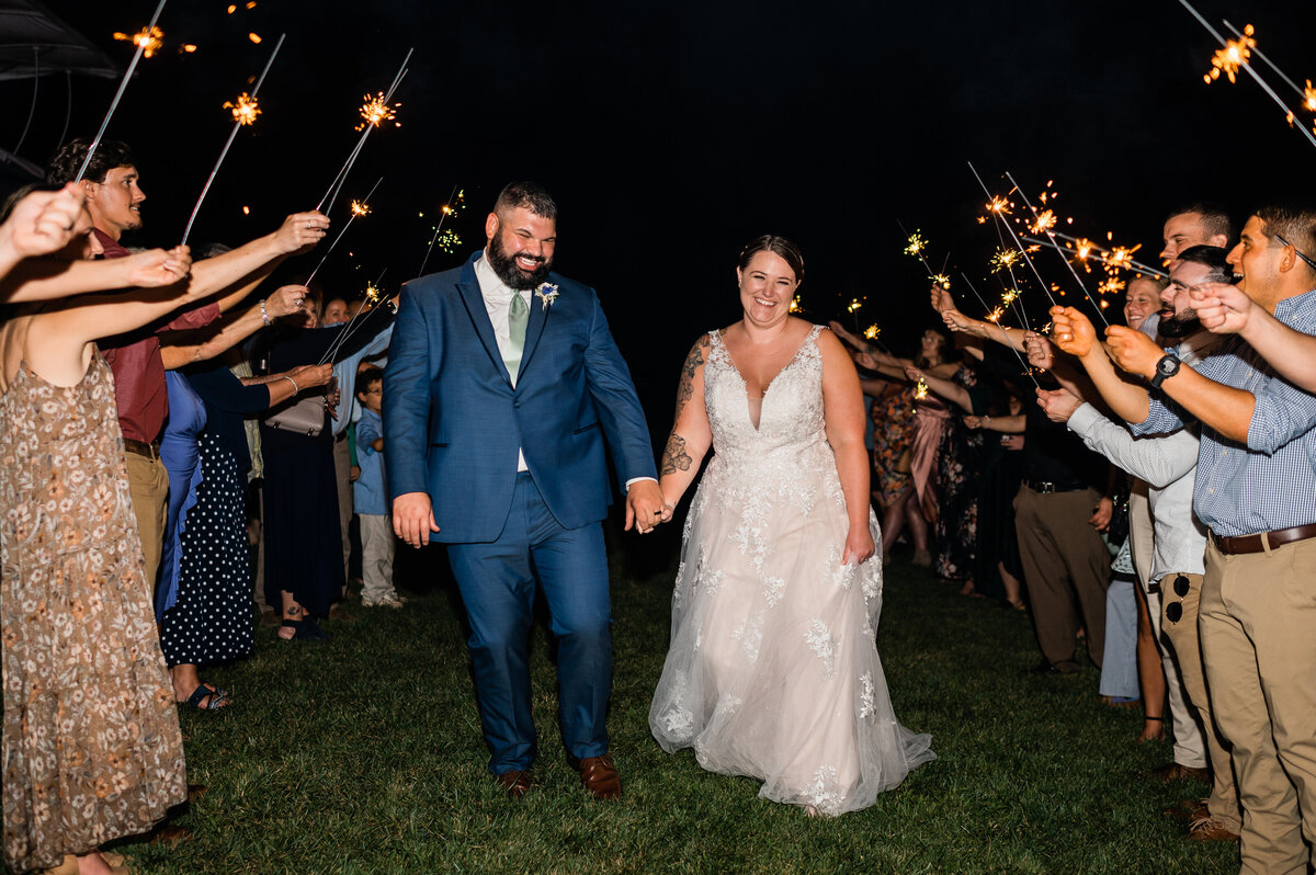 Bride and groom holding hands and walking through a tunnel of sparklers their guests are holding for their grand exit at Shenandoah wedding