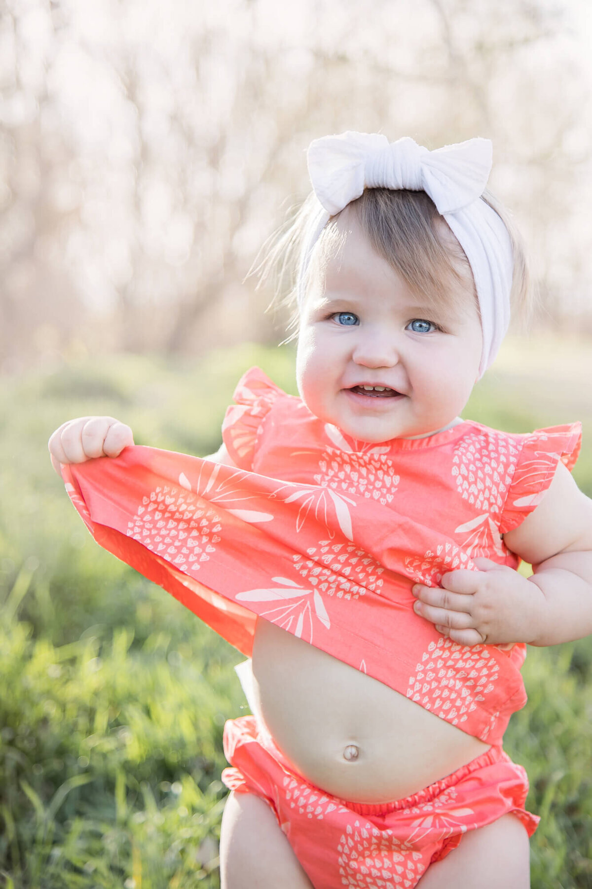 one year old baby girl standing in grass grabbing her dress playfully at a park with las vegas milestone photographer