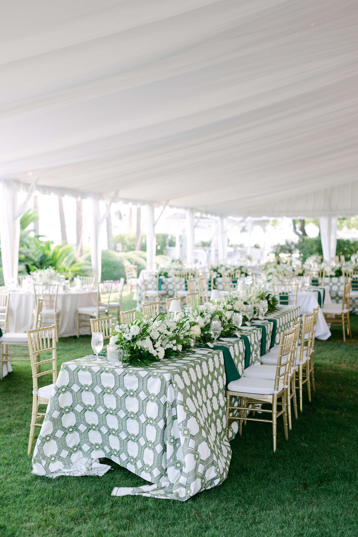 Tables and chairs sitting on soft green grass under a white tent.