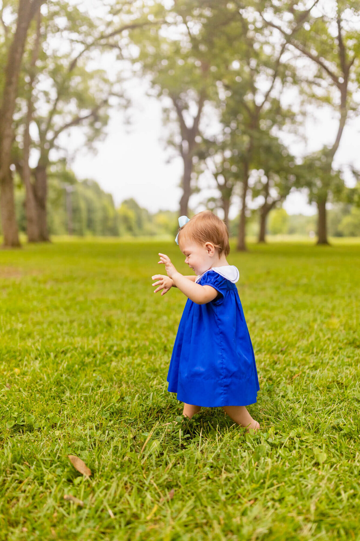 baby girl plays in a field of grass in a blue dress