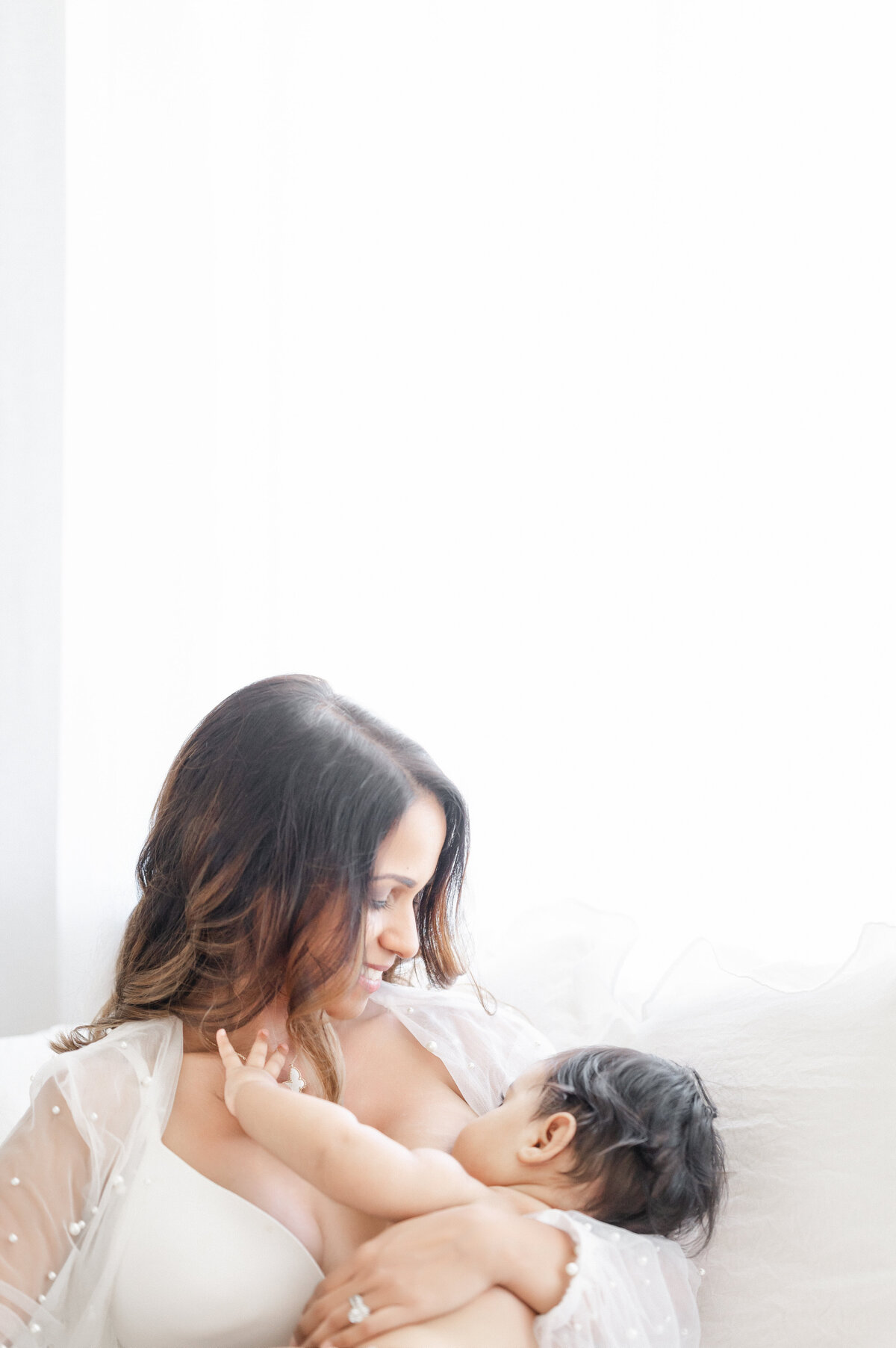 Luxury motherhood moment in Tampa studio: mother gently nursing baby in soft, editorial light