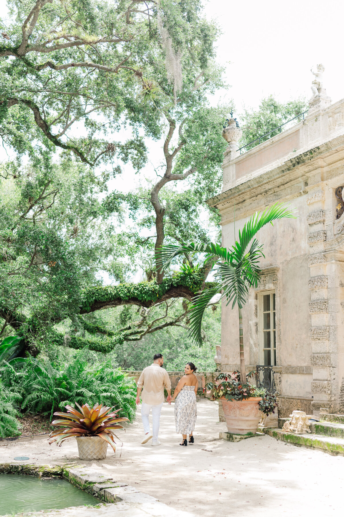 a couple holding hands while walking away from the camera at the vizcaya museum in miami