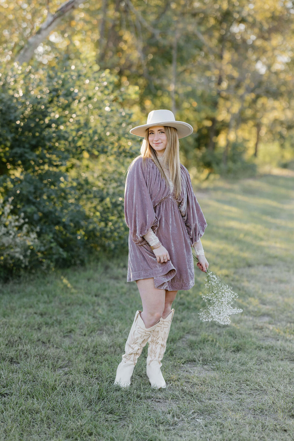Marshall, TX senior girl in pink velvet dress, white hat, and boots walking in east Texas park