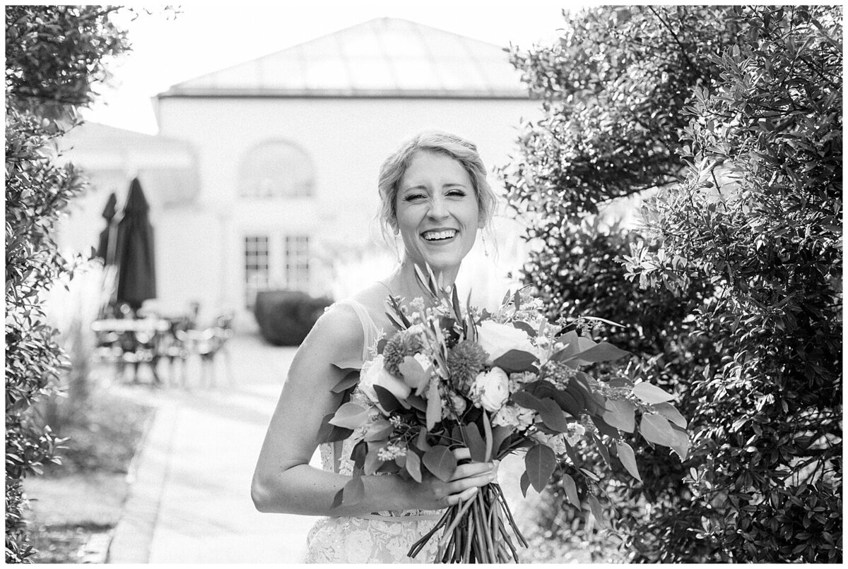 Candid black and white portrait of a bride laughing towards the camera holding her bouquet