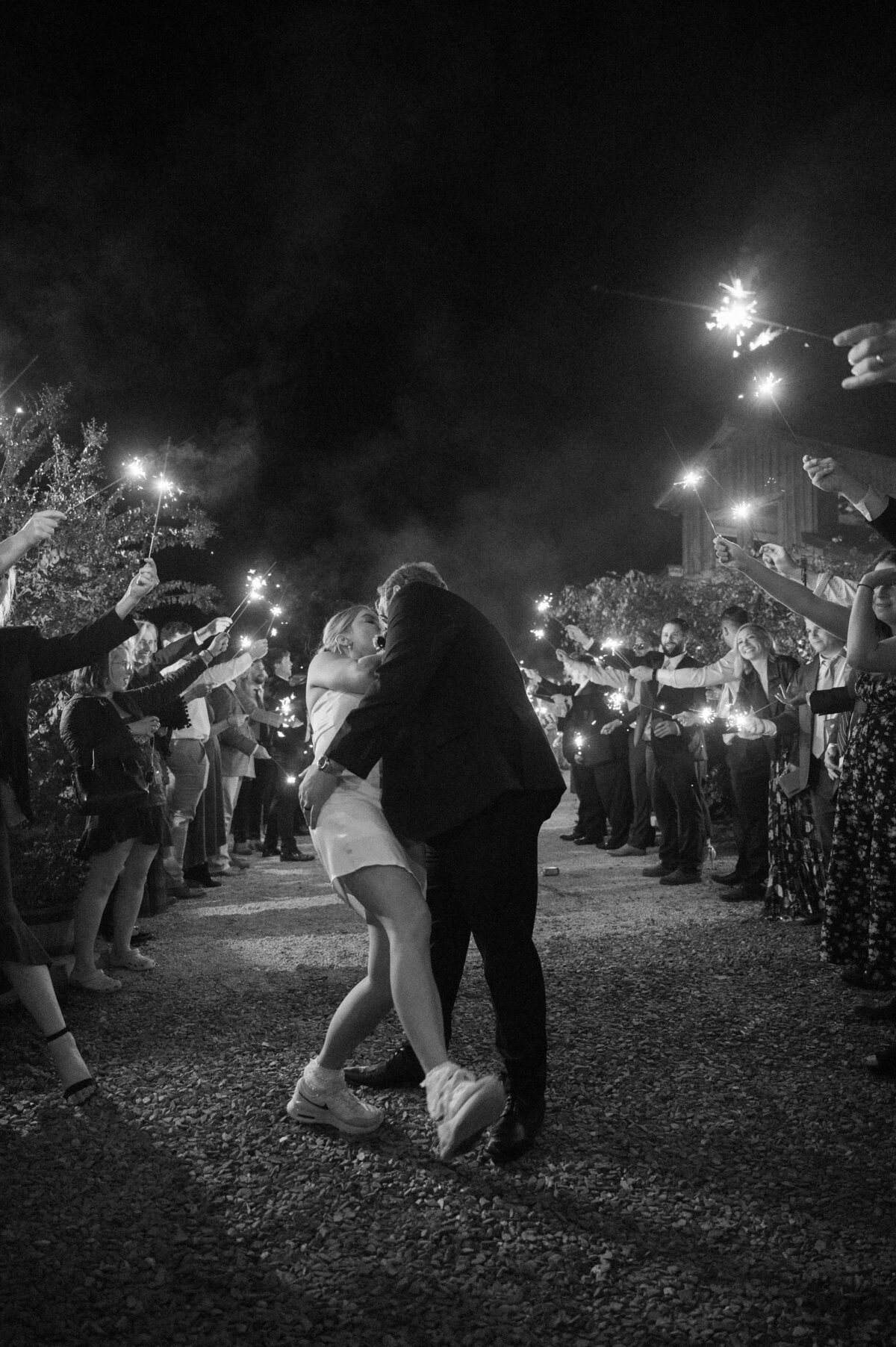 sparkler wedding exit with groom dipping his bride and kissing her as their wedding guests hold sparklers above them