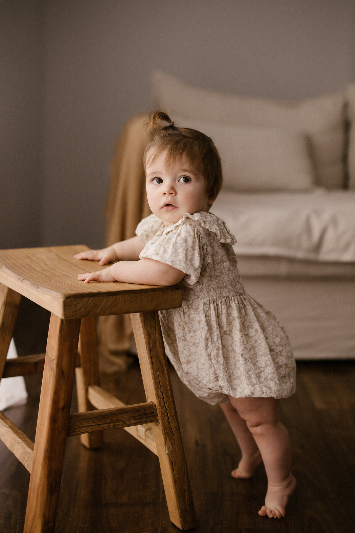 A little girl holding onto a stool during a baby photoshoot for a first birthday with aimee kelly photography in taranaki