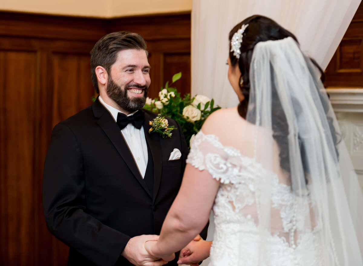Ottawa wedding photography showing a groom in a black tuxedo smiling widely as he looks at his bride at the altar.  Taken indoors at the Chateau Laurier hotel