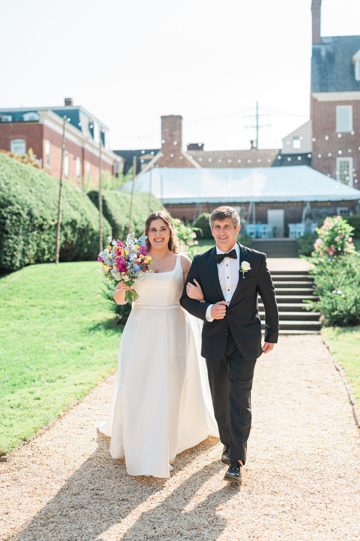 Two people walking down a gravel path with their arms linked