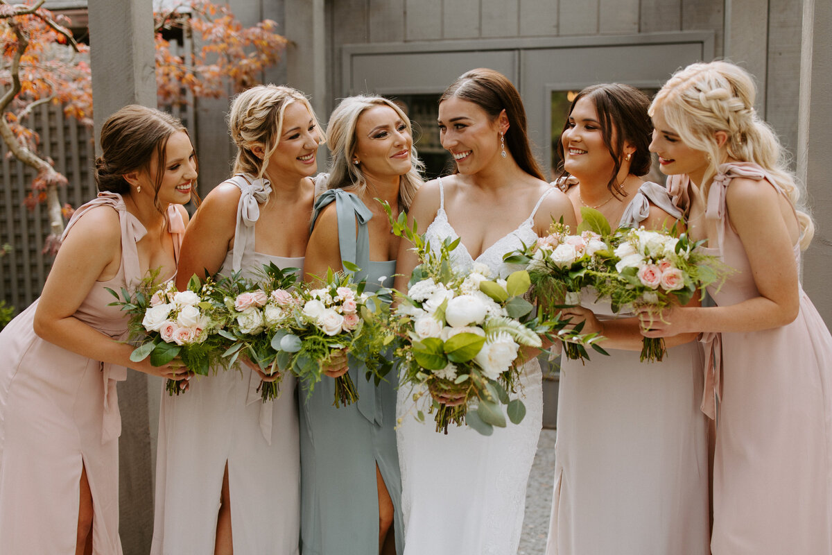 bride and wedding party standing together smiling while holding flowers