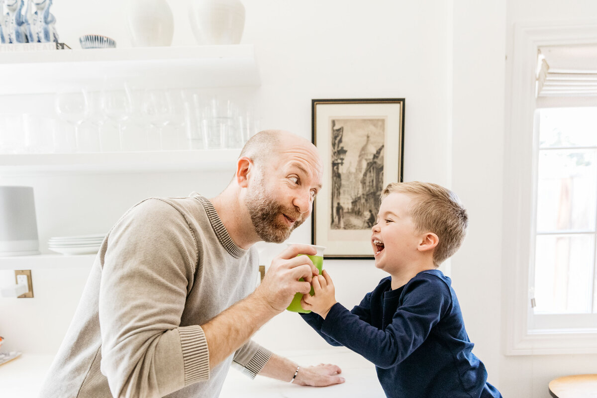 Dad and young son laughing and making goofy faces in the kitchen.