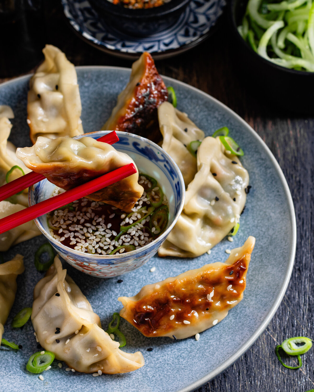 Vegetable gyoza held by chopsticks dipped into a bowl of soy dressing