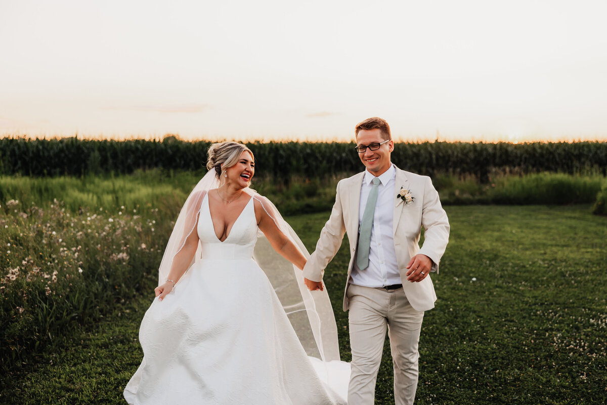A couple runs through an open field on their wedding day.