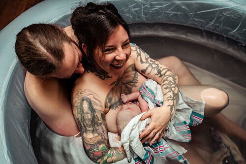 mother smiles holding newborn in birth tub at home birth