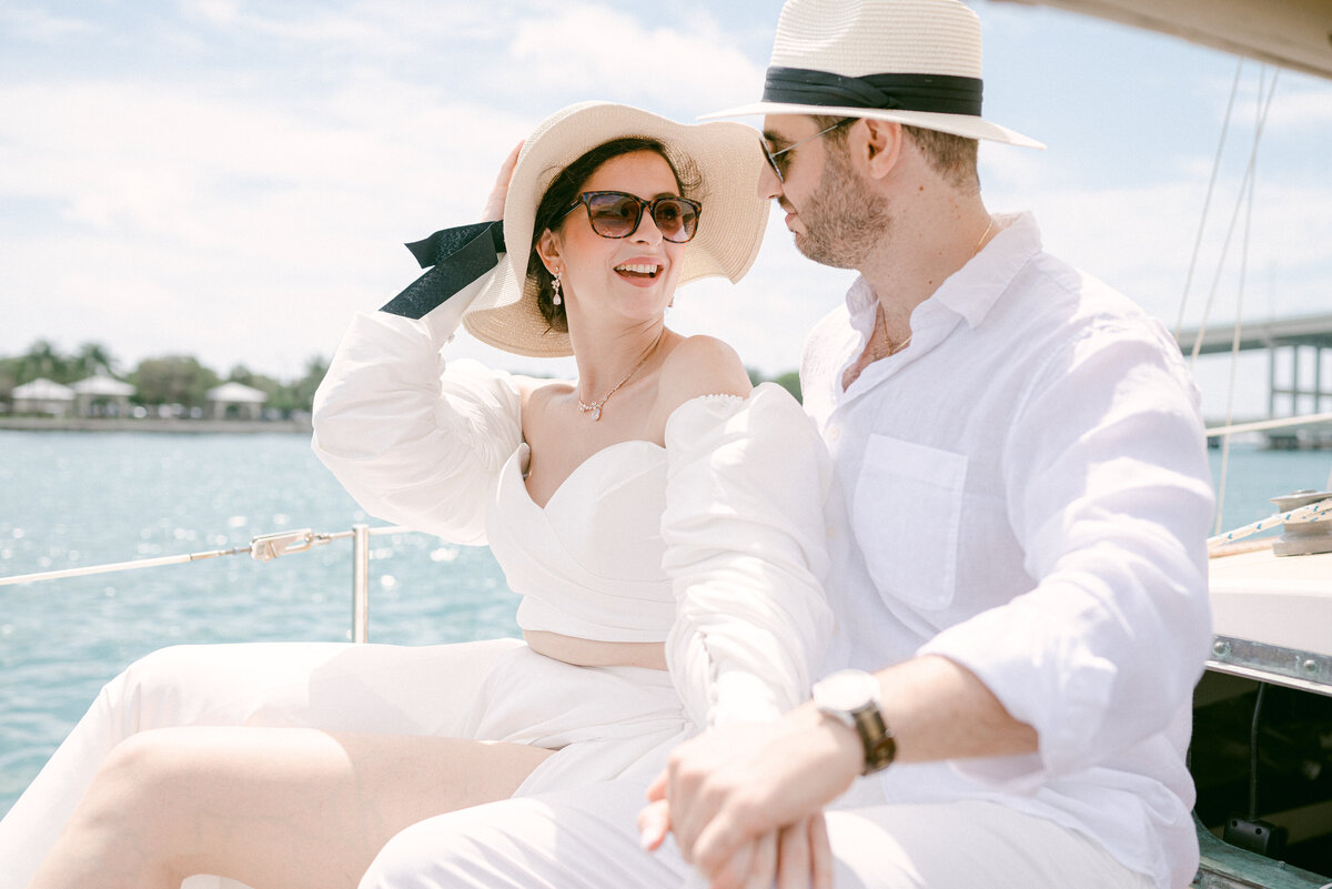 Couples holding sun hat on a boat holding hands and laughing together