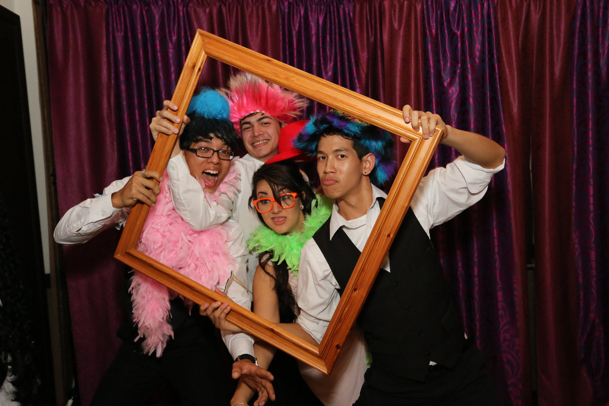 Fun loving foursome wearing hats and boas while holding a picture frame. Photobooth by Ross Photography, Trinidad, W.I..