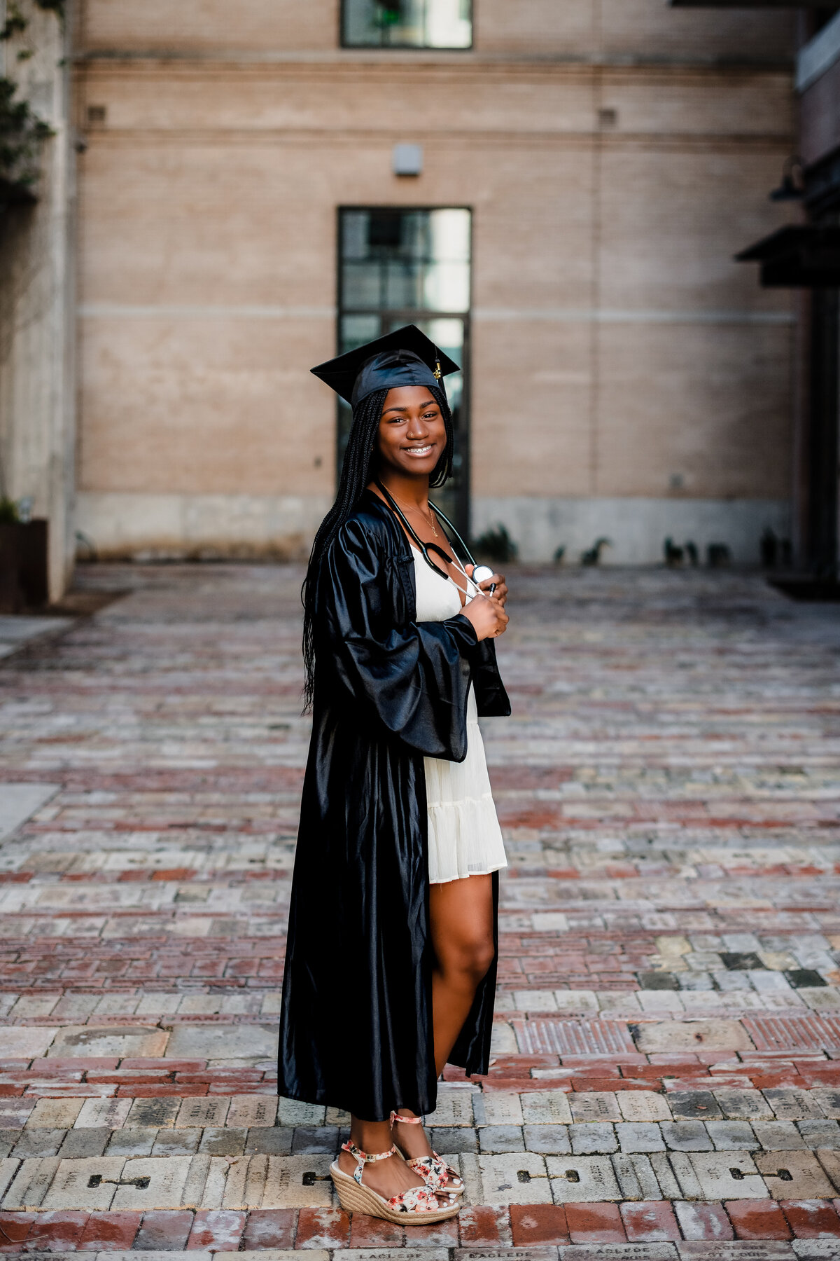 Steel High senior girl standing in black gown holding stethoscope around neck proudly at The Pearl.