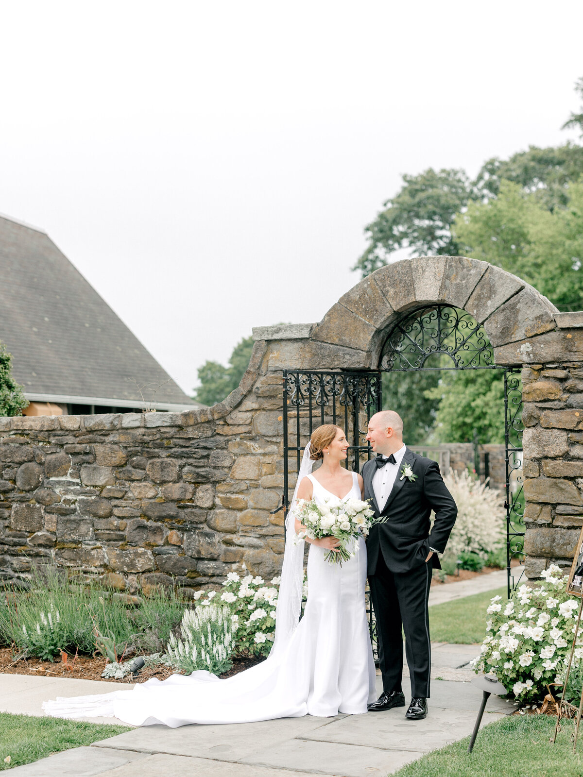 Bride and groom standing together smiling at each other in front of a stone gate