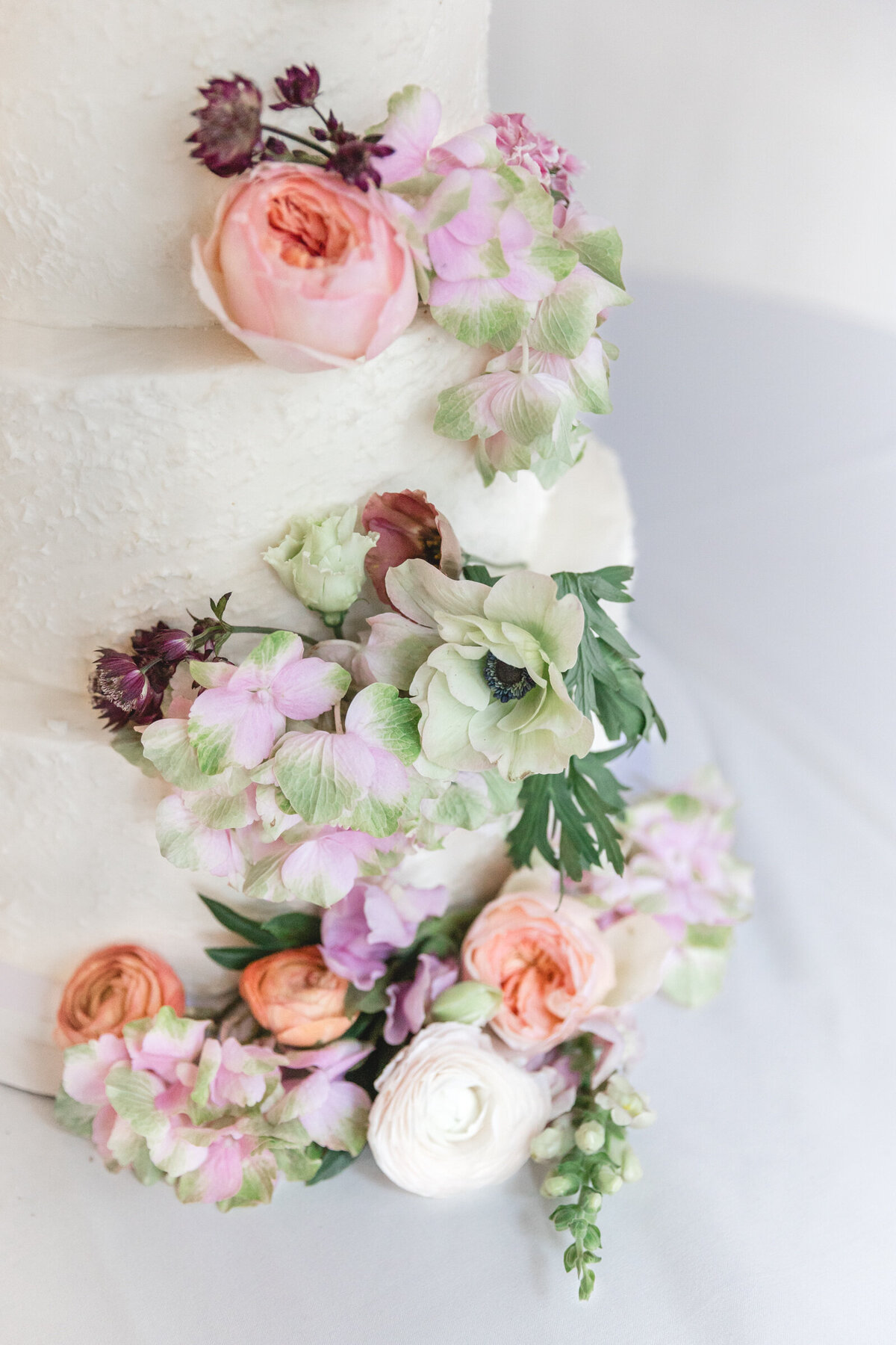 A close up of peach, green, and lavender flowers on a wedding cake