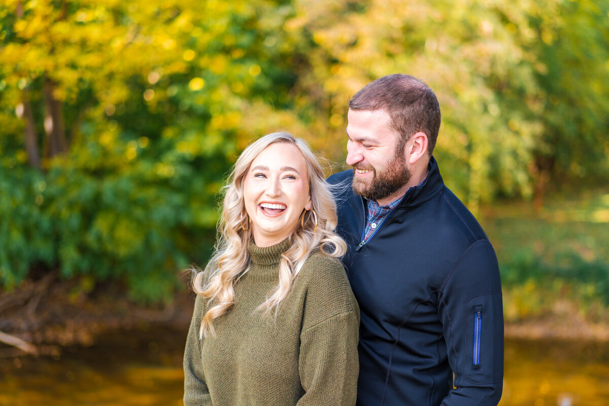 Husband holds his wife and they laugh together in front of fall foliage in Canal Winchester, Ohio.