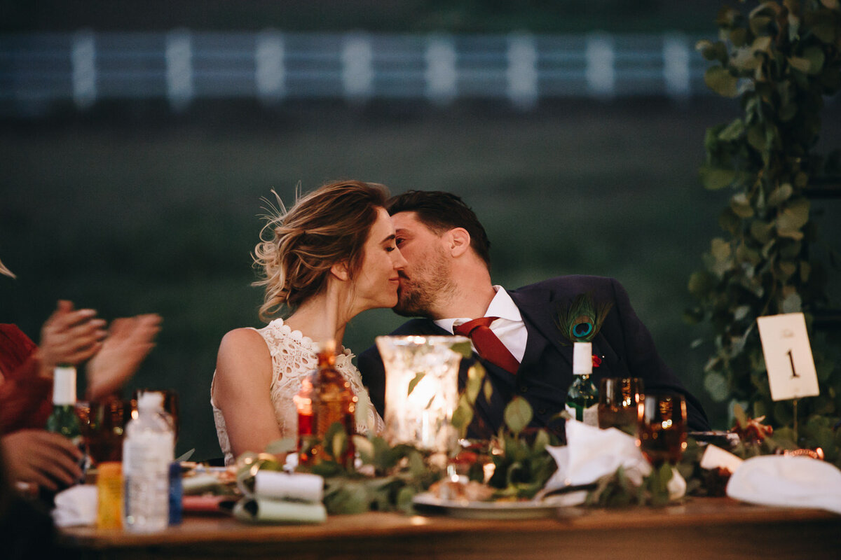 Ali and Brian kiss while sitting at their table.