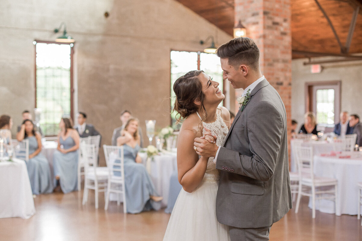 The bride and groom smile lovingly at each other during their first dance as man and wife as their seated guests watch.