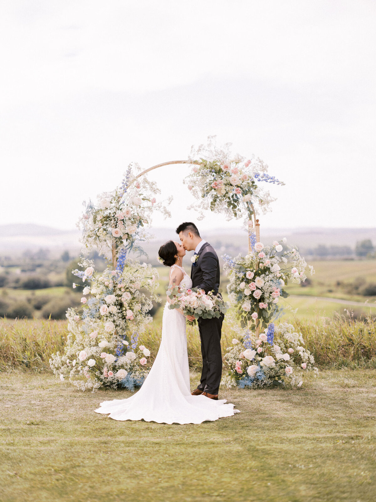 Couple standing in front of elegant ceremony arch, covered in white and blue florals styled by Melissa Dawn Event Designs, a unique and modern wedding planner based in Calgary, Alberta. Featured on the Brontë Bride Vendor Guide.