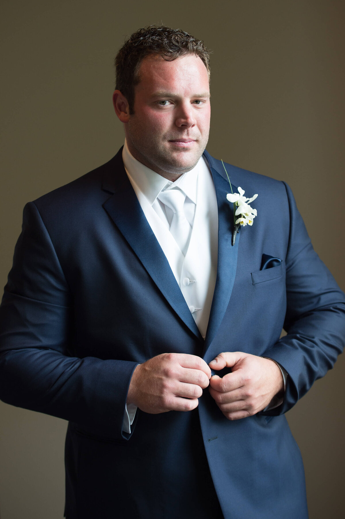 a portrait of a handsome groom buttoning his jacket as he gets ready for his Ottawa wedding photography at the Brookstreet Hotel wedding venue and The Marshes