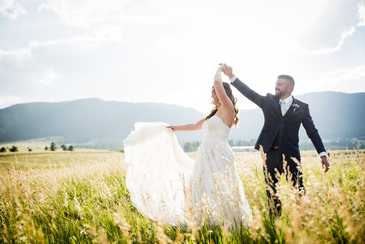 A groom twirls his bride in a field at golden hour.
