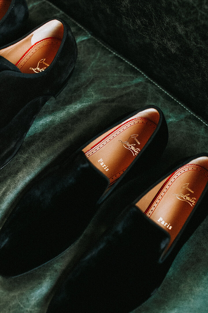 Three Black suede Christian Louboutin loafers atop a green leather couch.