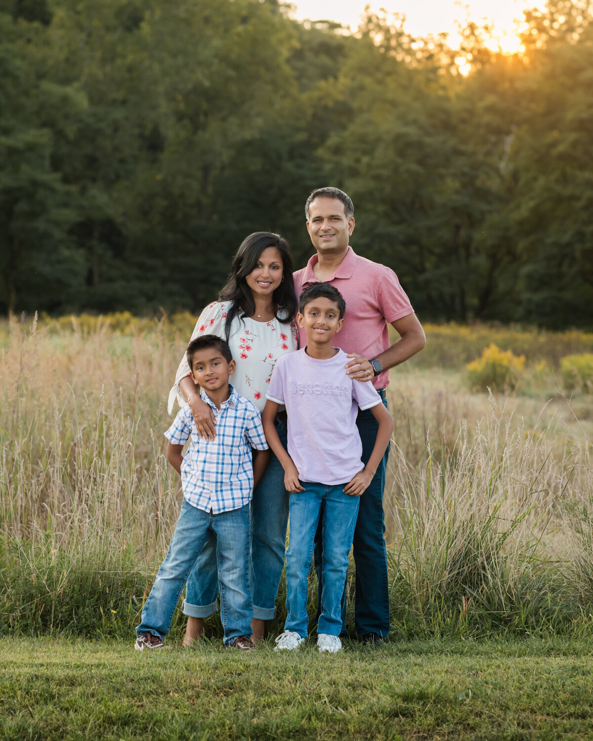 mom dad and two sons posing in field for family photos 