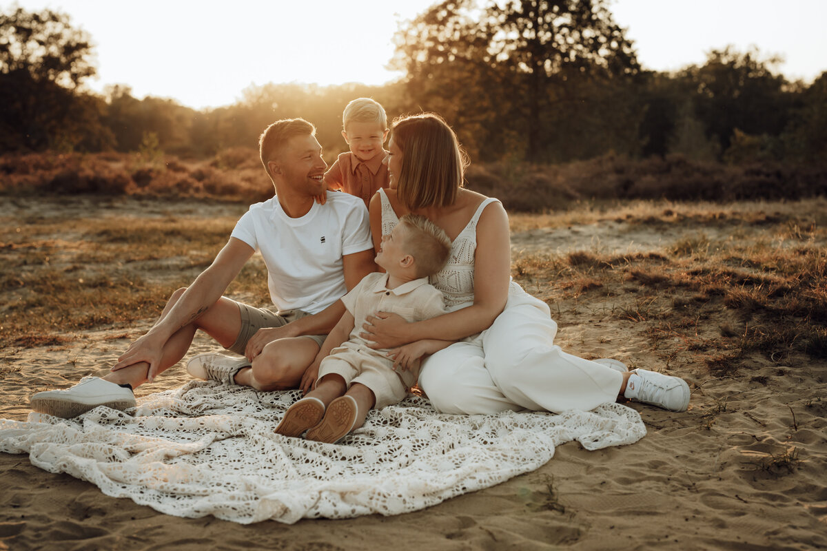 Gezin zit op dekentje in de heide tijdens golden hour voor gezinsshoot