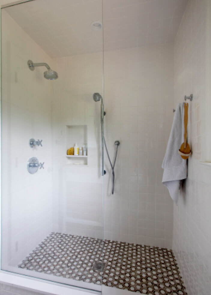 Bathroom designers in Westwood design a walk-in shower with simple white tile and stone mosaic flooring, blending timeless style with modern functionality.